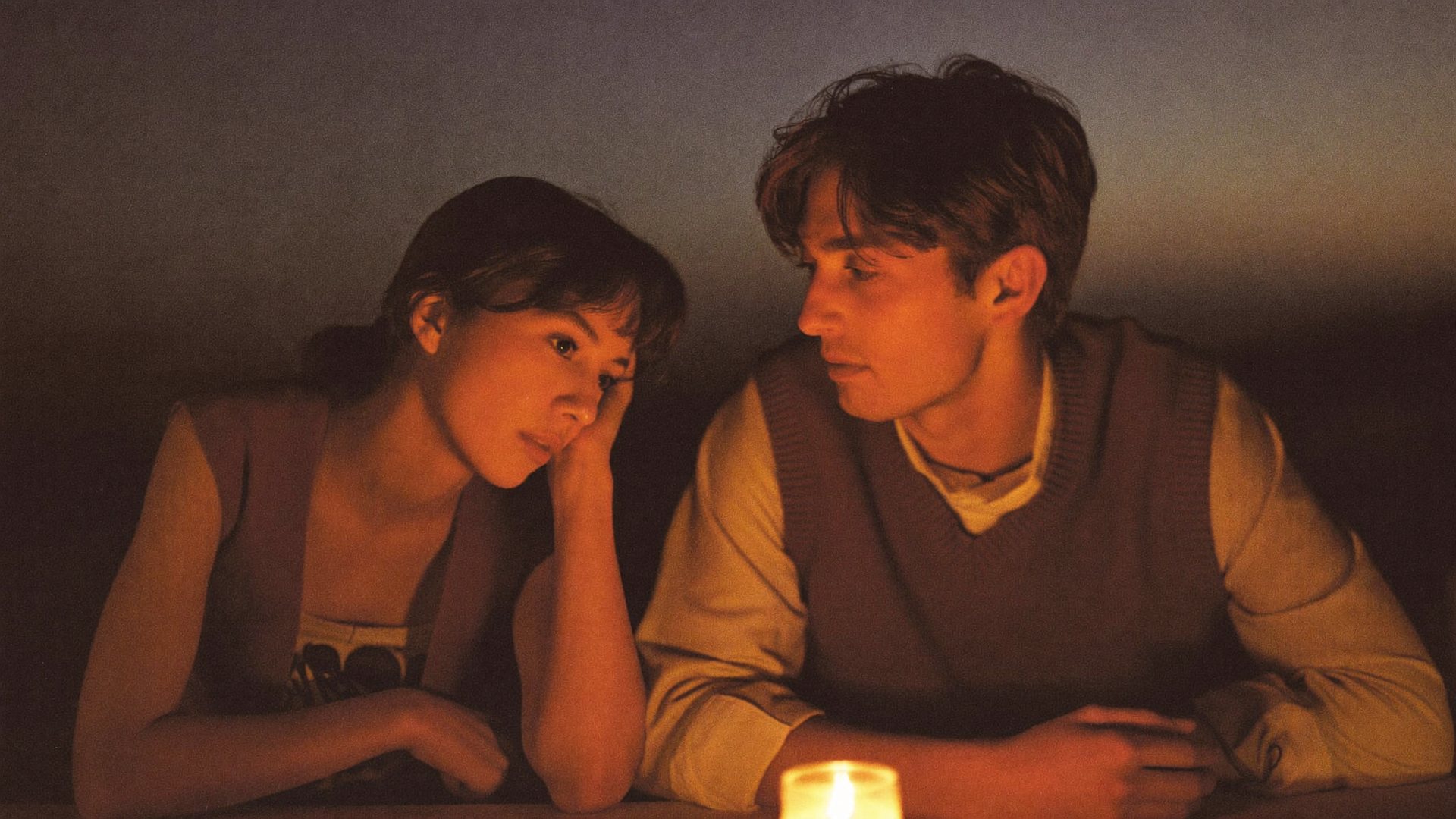 A woman and a man leaning close together in warm candlelight