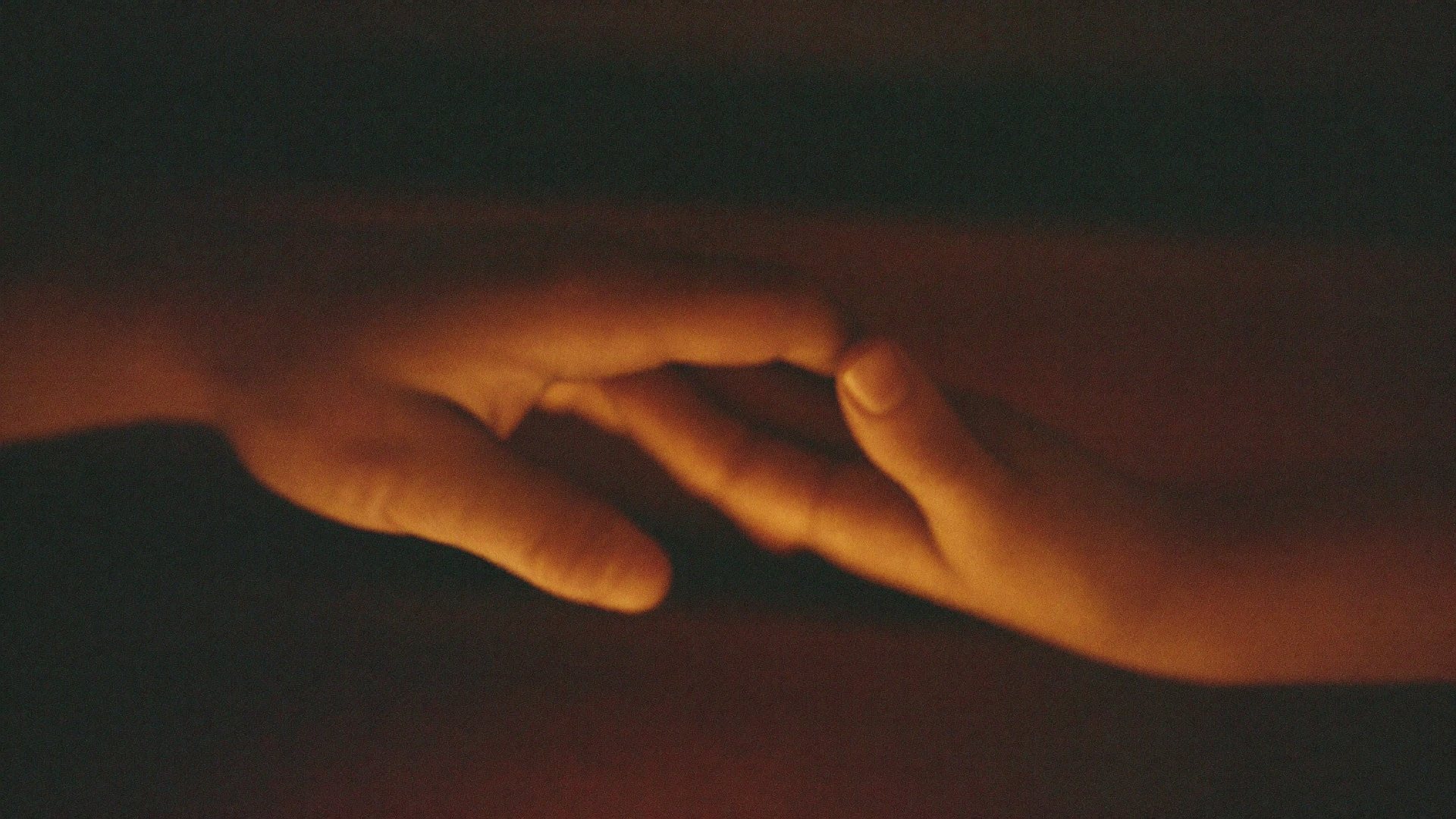 Two hands reaching toward one another in warm lamplight